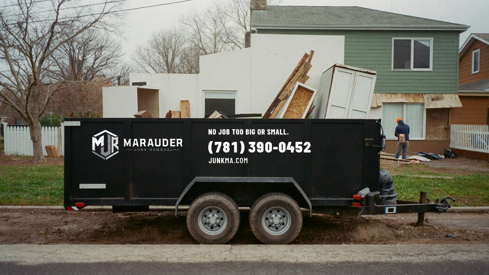 Black Marauder dump trailer loaded with renovation debris and old cabinets outside a house under construction