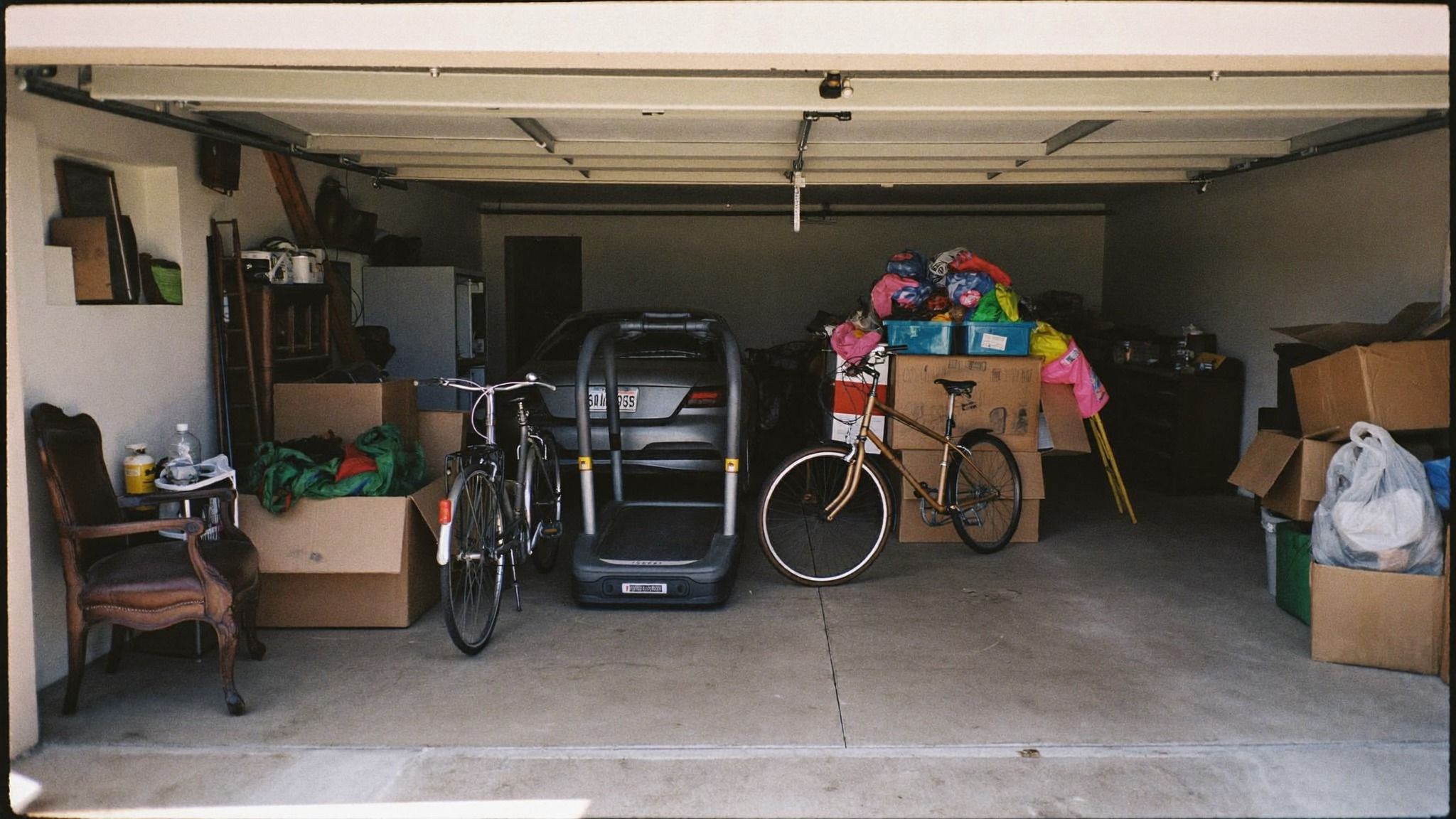 Two-car garage packed with boxes, bikes, a treadmill, an armchair and bags of household items
