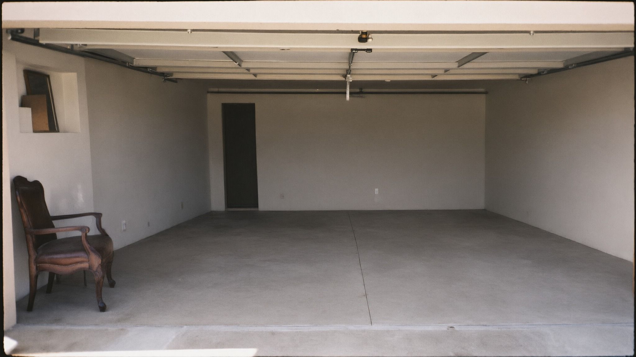 Empty, swept two-car garage with a bare concrete floor and one armchair by the wall