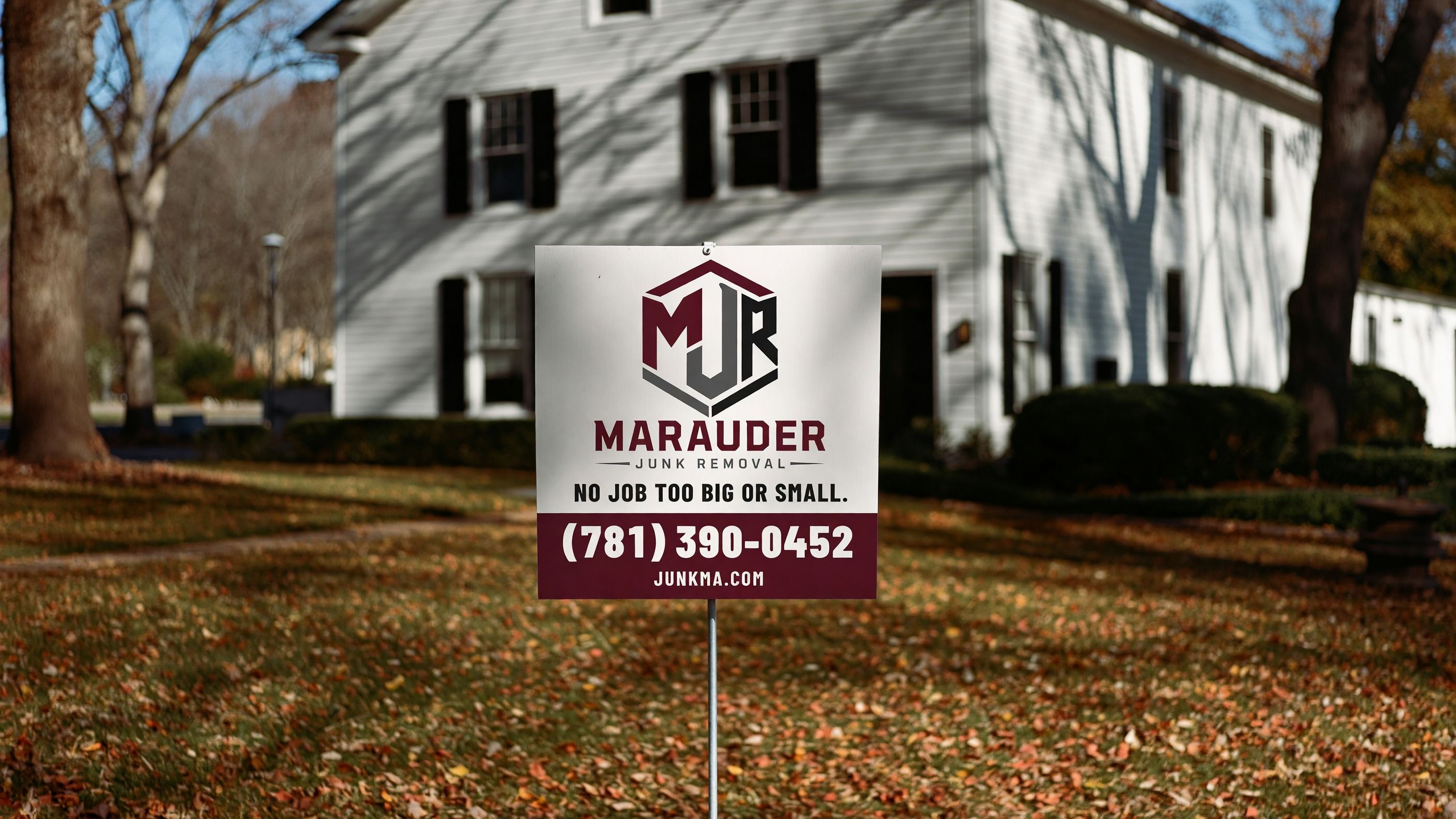 Marauder Junk Removal yard sign with the phone number on a leaf-covered lawn in front of a white house